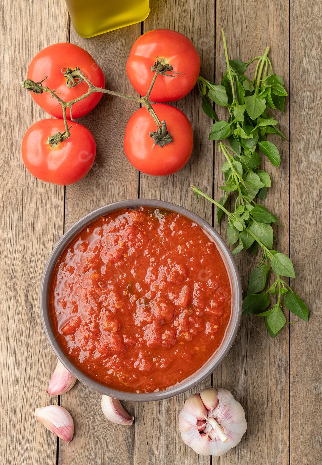 Molho de tomate, tomate, alho, azeite e ervas sobre a mesa de madeira.