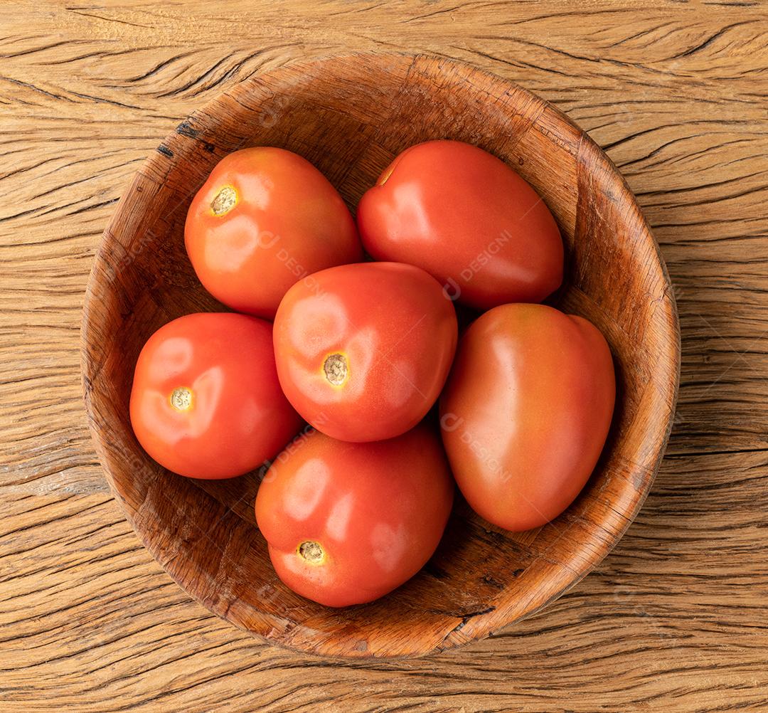 Tomates vermelhos em uma tigela sobre a mesa de madeira.