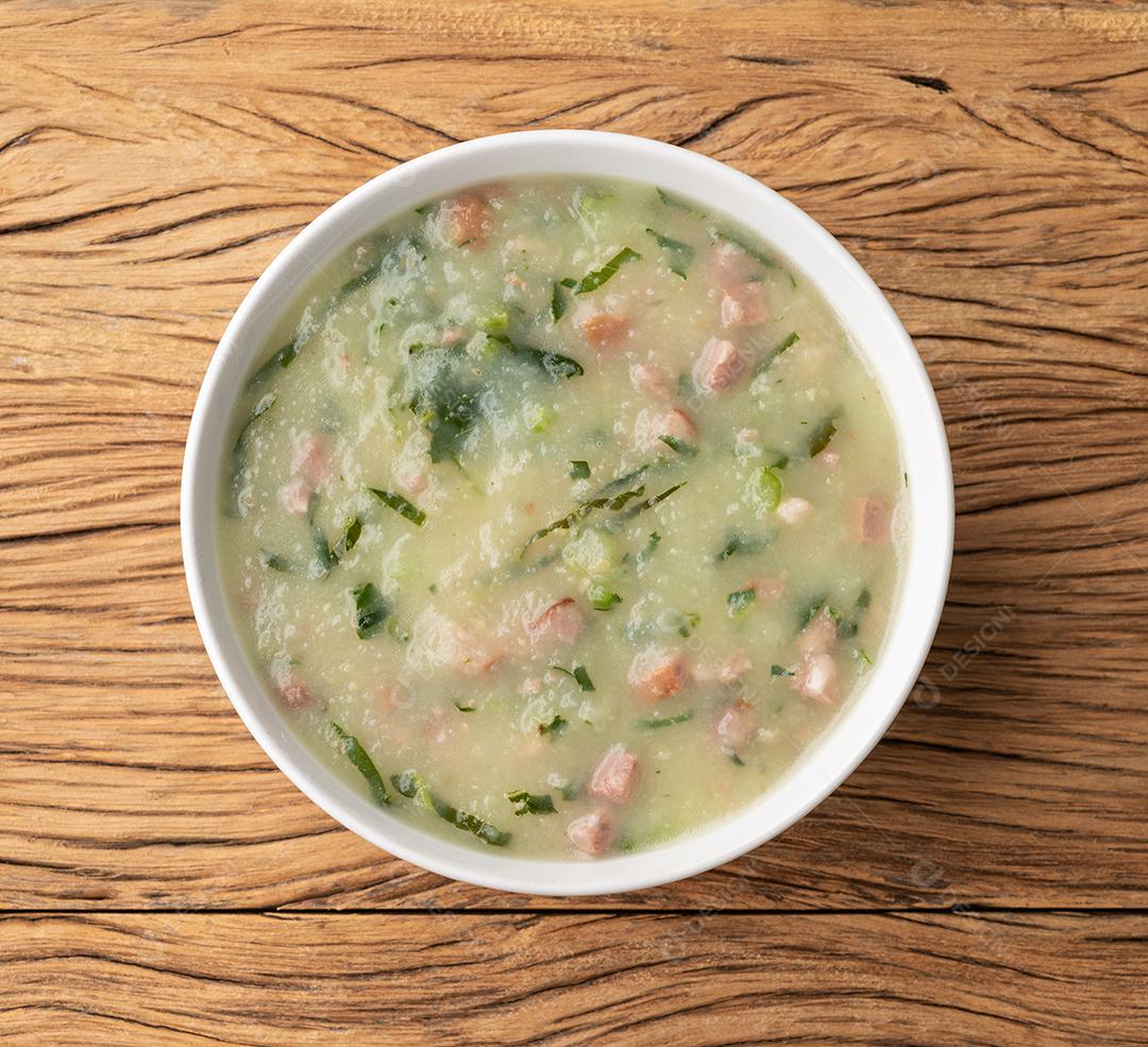 Sopa verde portuguesa tradicional com batata, couve verde e salsicha numa tigela sobre mesa de madeira