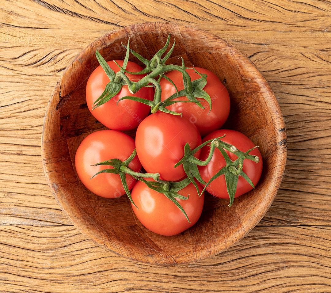 Tomates vermelhos em uma tigela sobre a mesa de madeira.