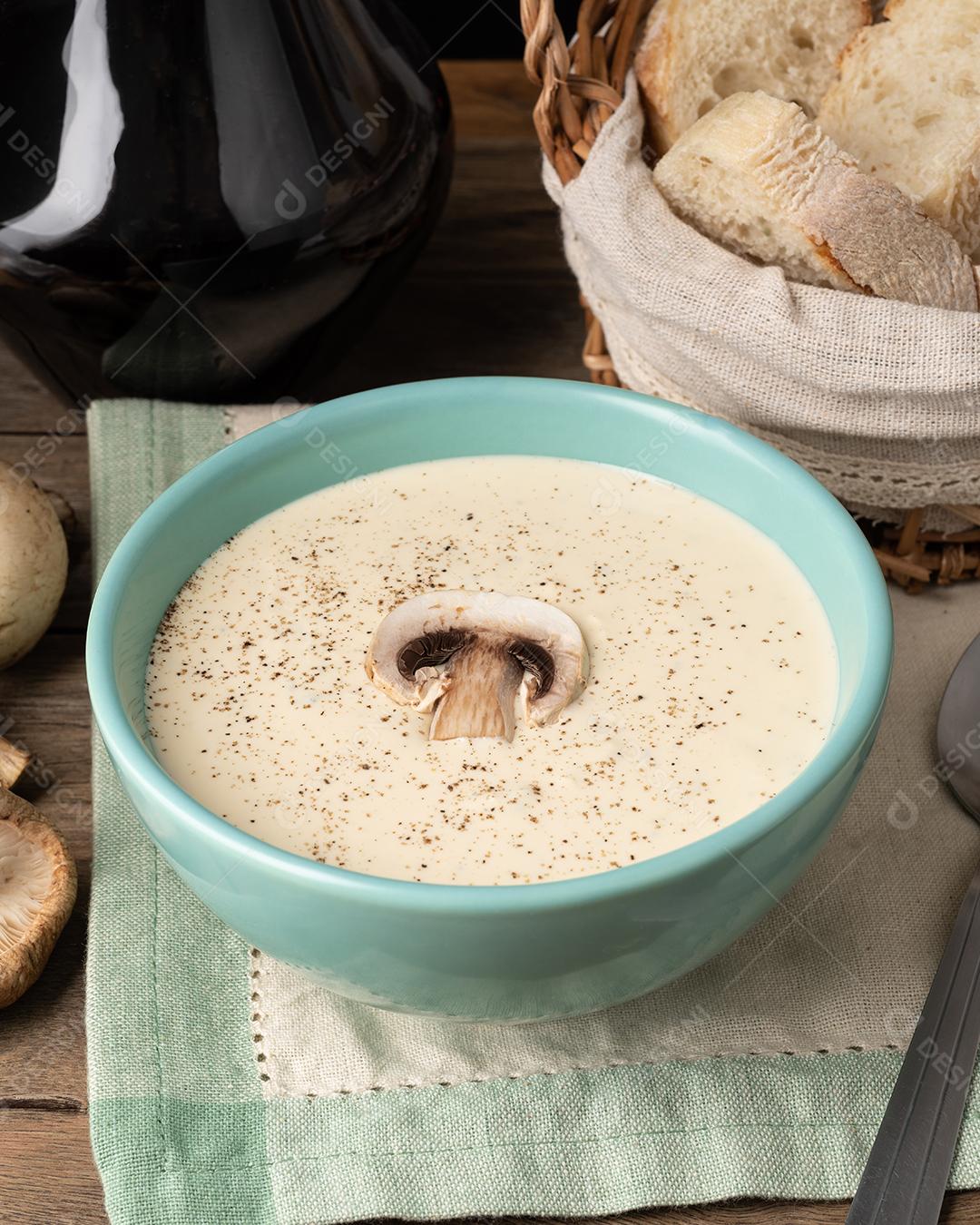 Sopa de cogumelos em uma tigela com fatias de pão e vinho sobre a mesa de madeira.