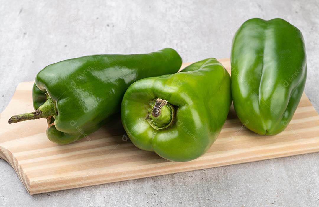 Três pimentões verdes sobre placa de madeira.