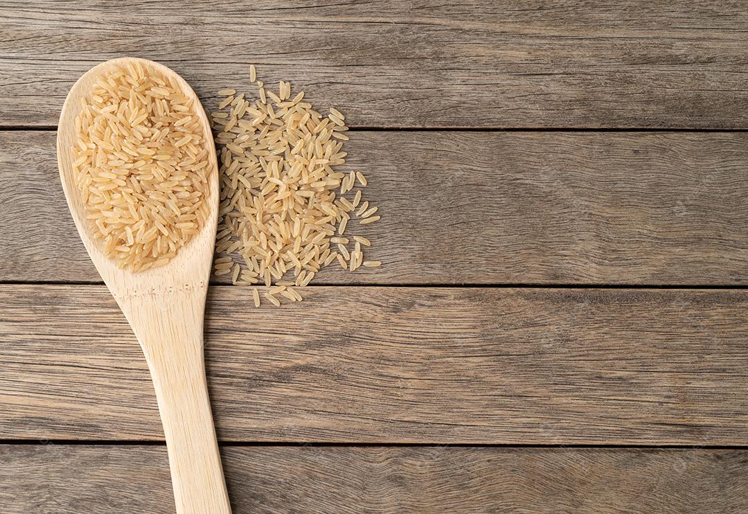 Arroz integral cru em uma colher sobre a mesa de madeira com espaço de cópia.