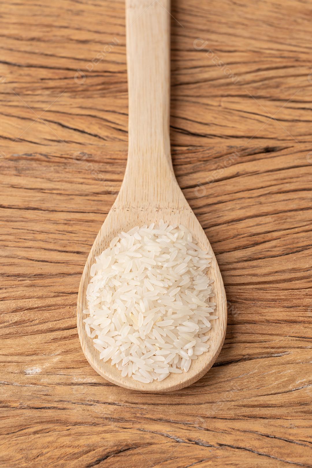 Arroz branco cru em uma colher sobre a mesa de madeira.