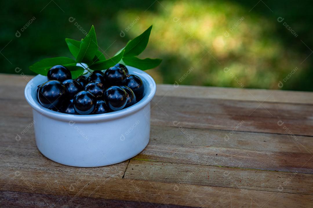 Jabuticabas over a white bowl on a madeira table