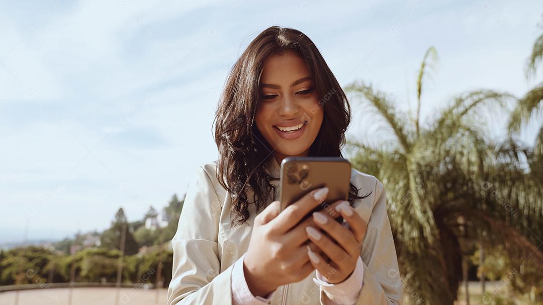 Beautiful latin young woman using smartphone while standing in the city st