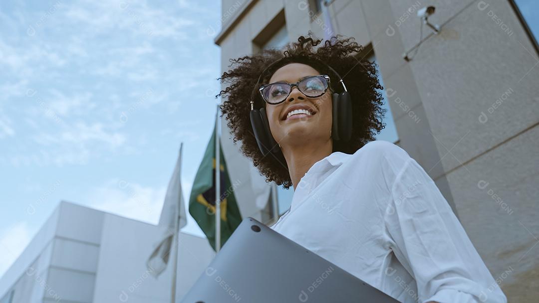 Low angle view of smiling Latin businesswoman holding laptop and