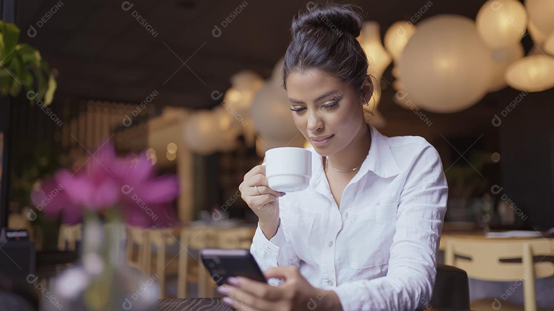Linda garota latina usando seu celular no café.