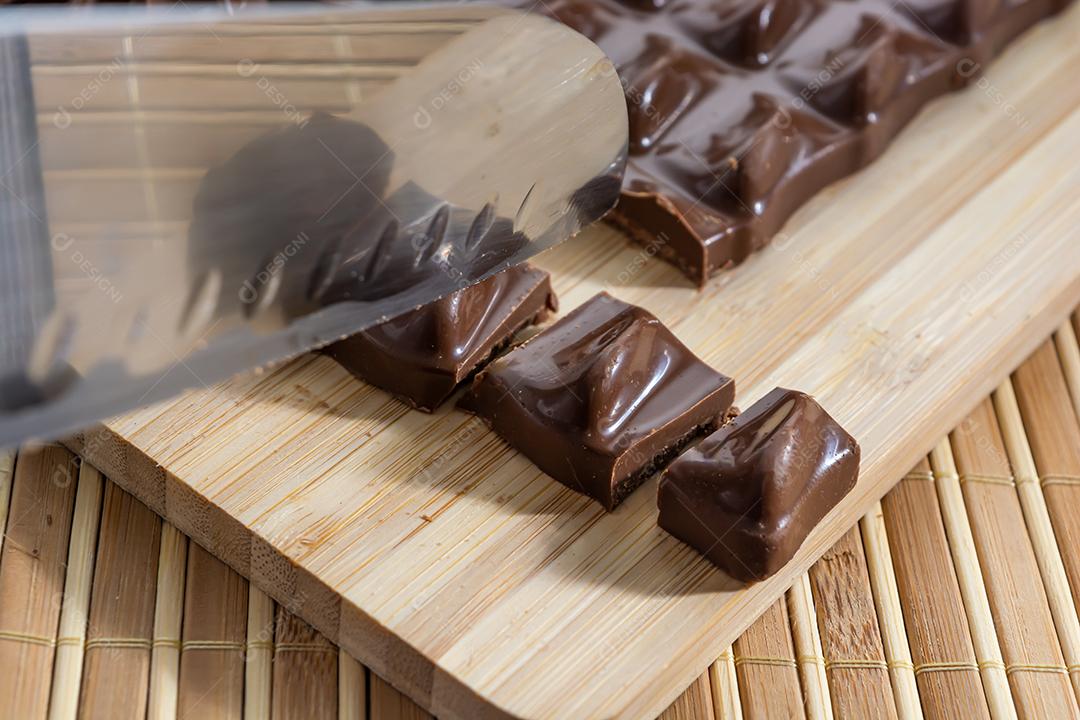 cortando pedaços de chocolate ao leite em uma tábua de madeira com