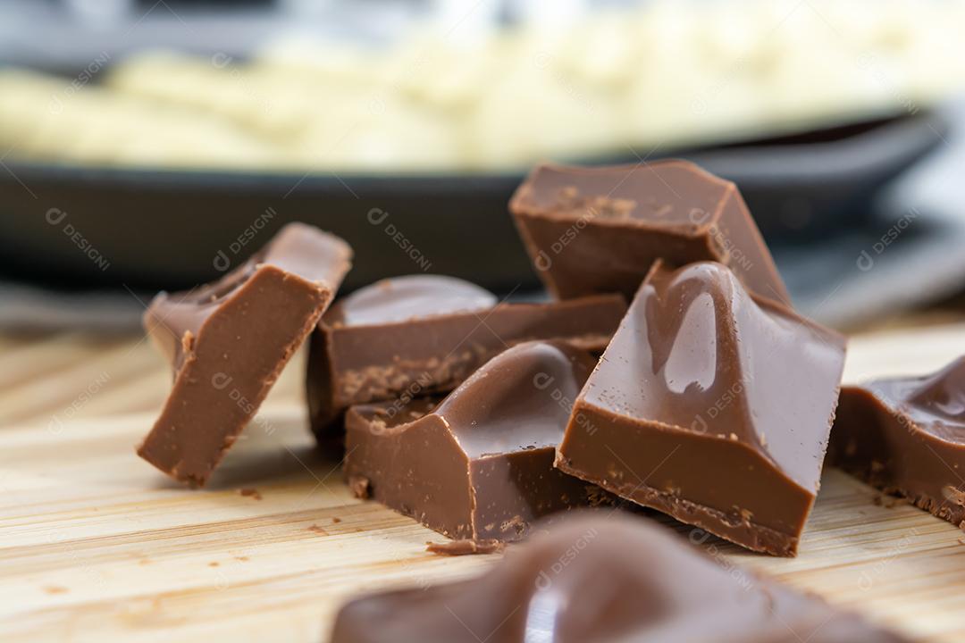 Pedaços de chocolate ao leite e barra de chocolate no fundo, sobre madeira