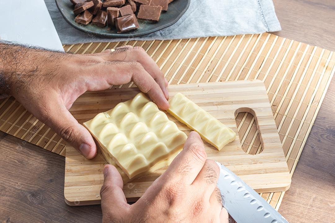 homem cortando barras e pedaços de chocolate branco com uma faca