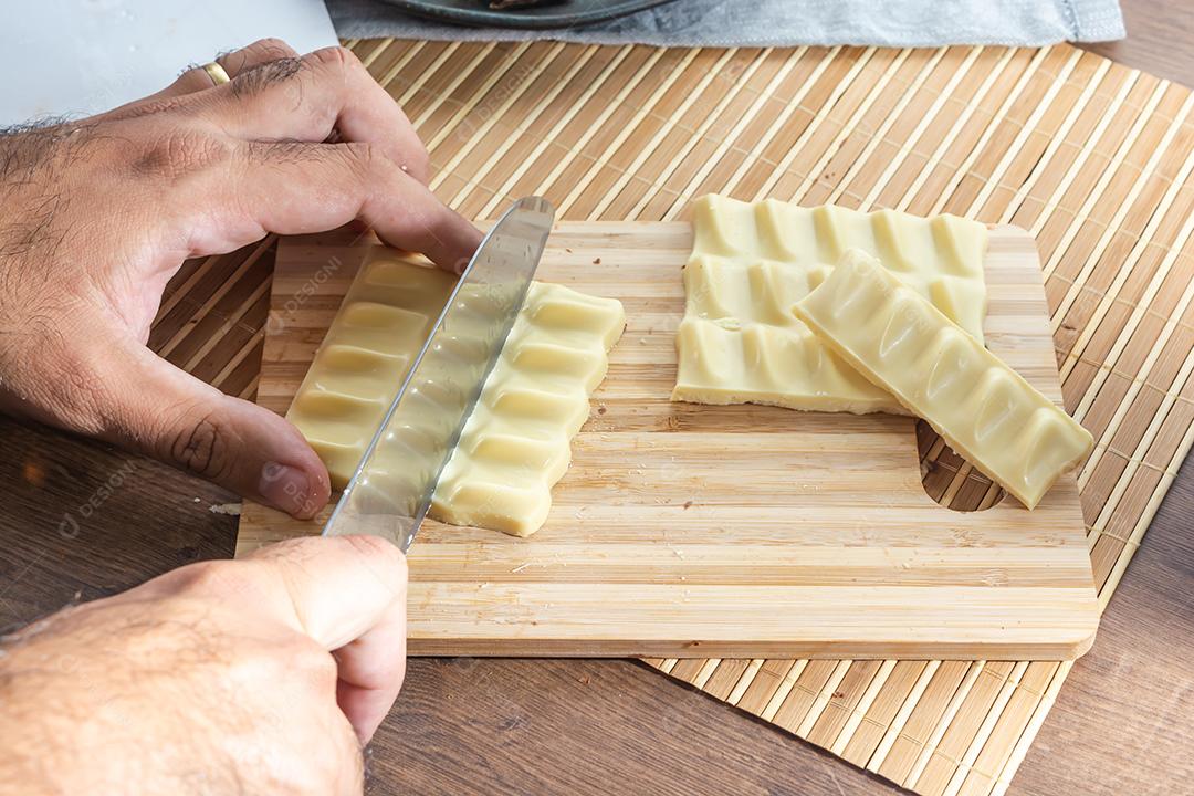 homem cortando barras e pedaços de chocolate branco com uma faca em um cu