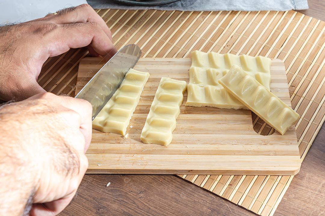 homem cortando barras e pedaços de chocolate branco com uma faca em um cu