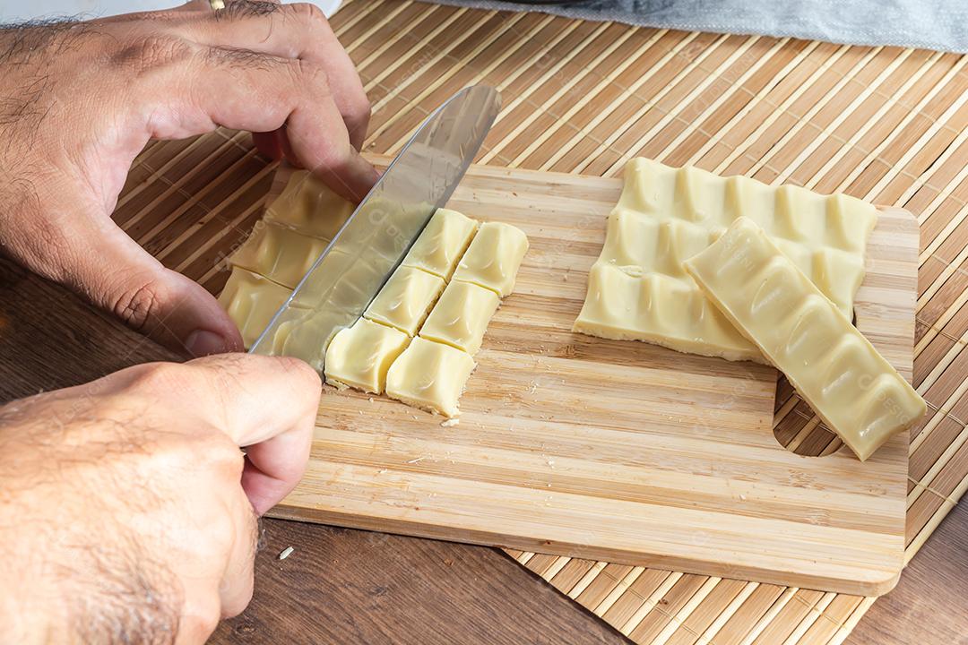 homem cortando pedaços de chocolate branco na tábua de madeira