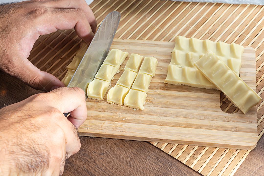 homem cortando pedaços de chocolate branco na tábua de madeira