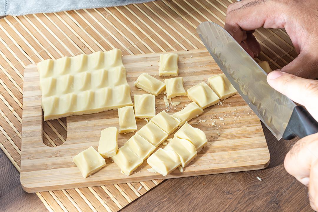 homem cortando pedaços de chocolate branco na tábua de madeira