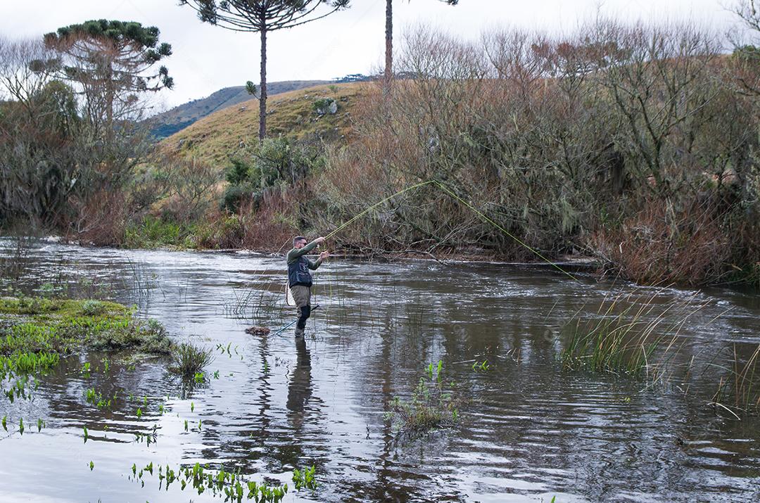 Pescador pesca truta arco-íris na montanha em belas paisagens.