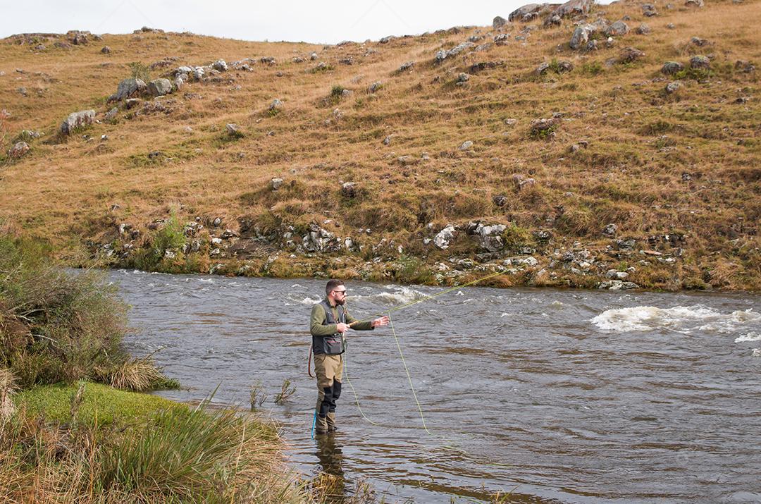 Pescador pesca truta arco-íris na montanha em belas paisagens.