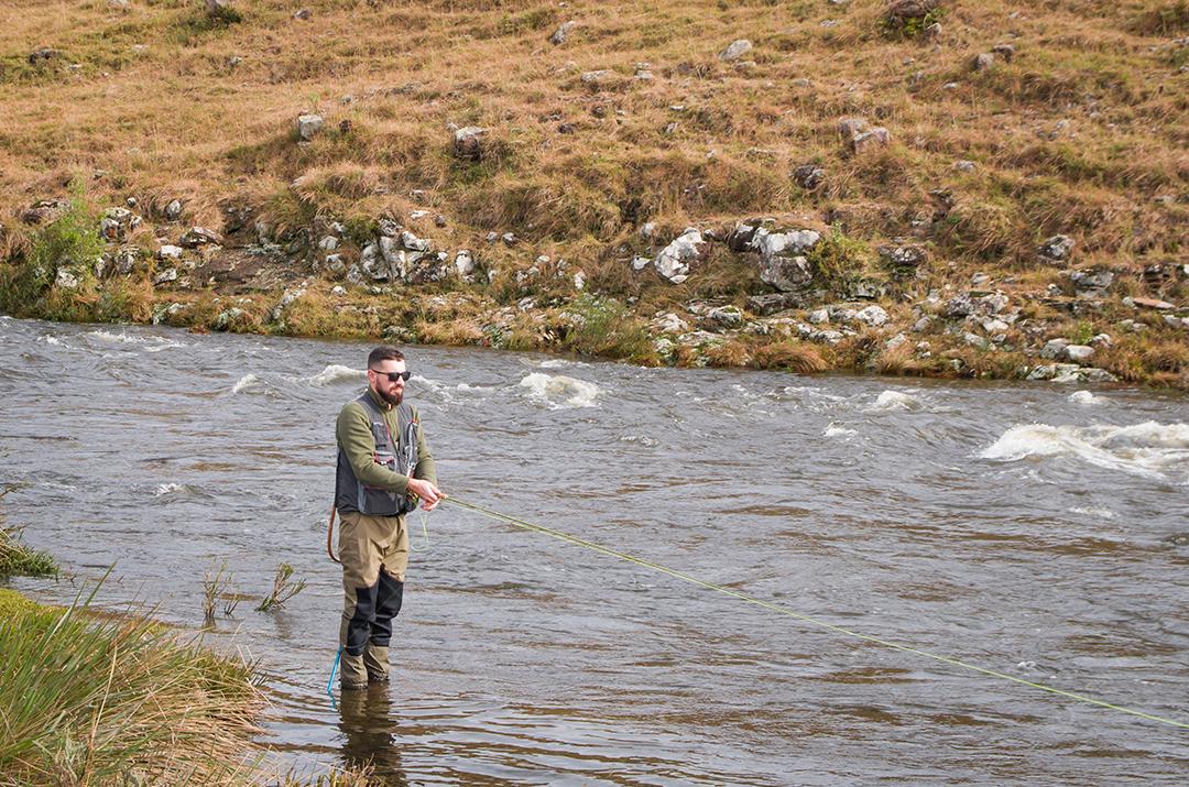 Pescador pesca truta arco-íris na montanha em belas paisagens.