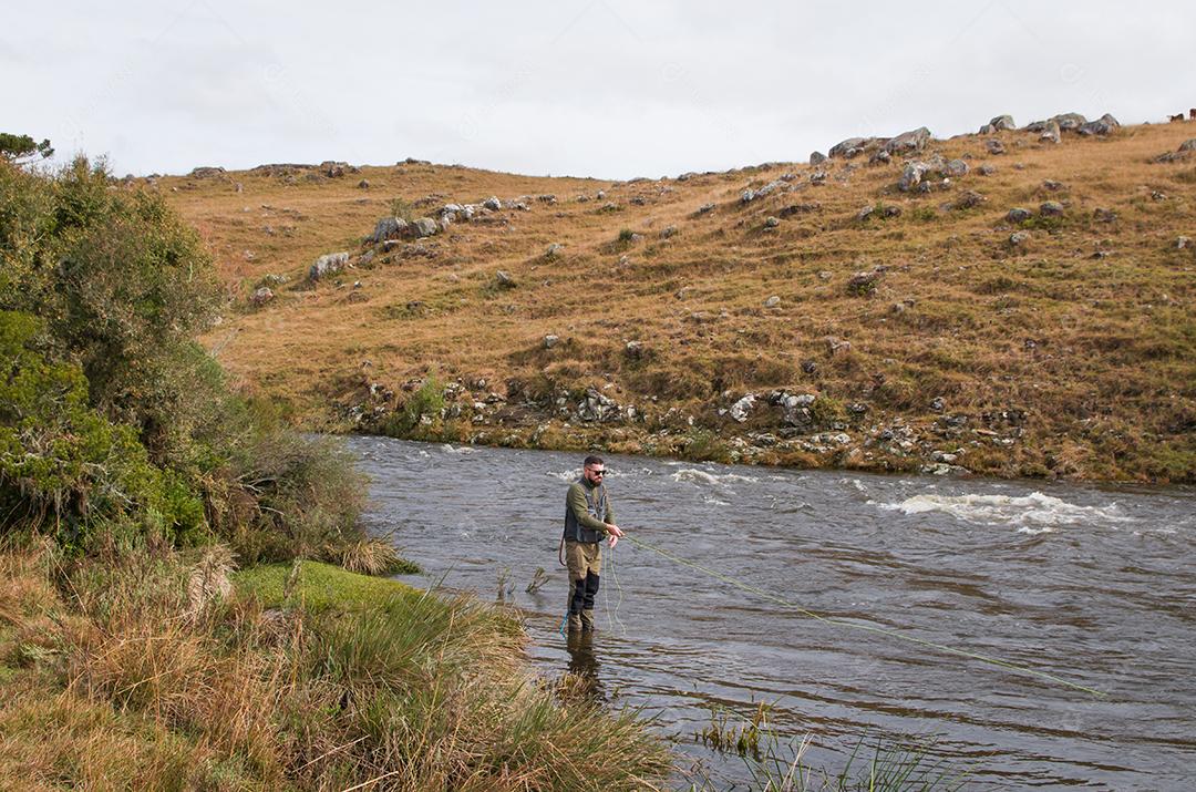 Pescador pesca truta arco-íris na montanha em belas paisagens.