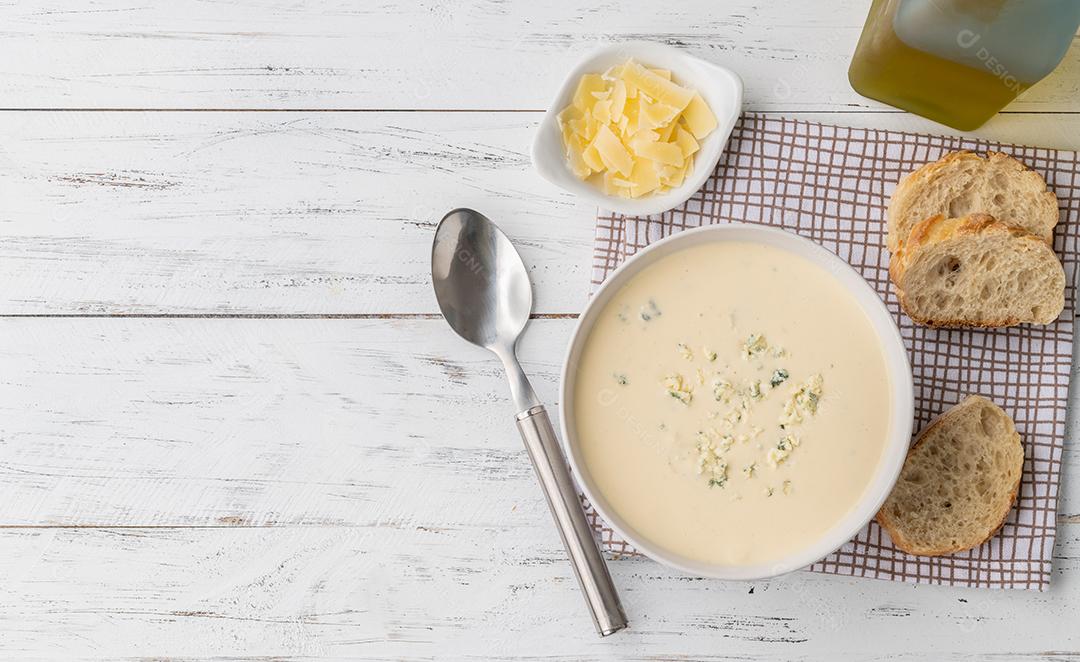 Sopa de queijo em uma tigela com fatias de pão e temperos sobre madeira