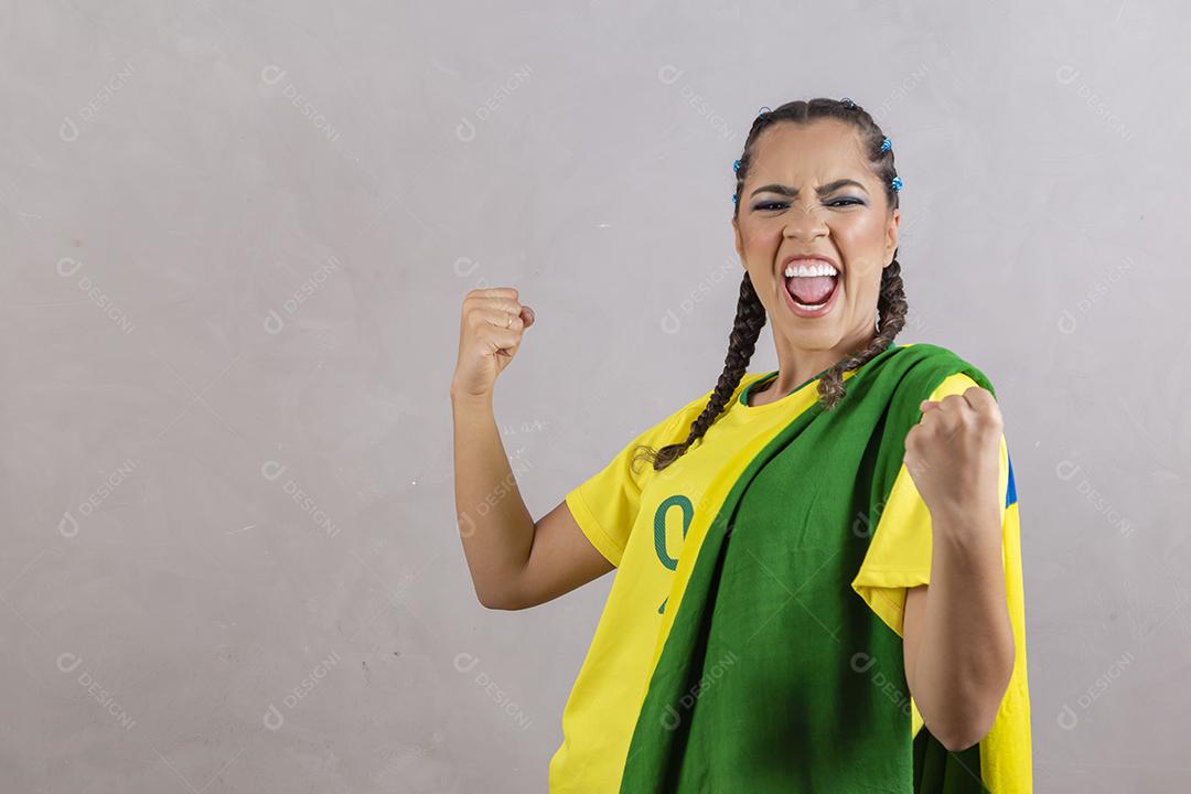 Torcedora brasileira. Fã brasileira comemorando partida de futebol em fundo cinza.