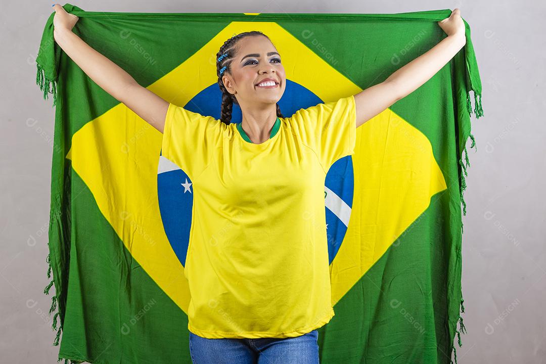 Torcedora brasileira. Fã brasileira comemorando partida de futebol em fundo cinza.