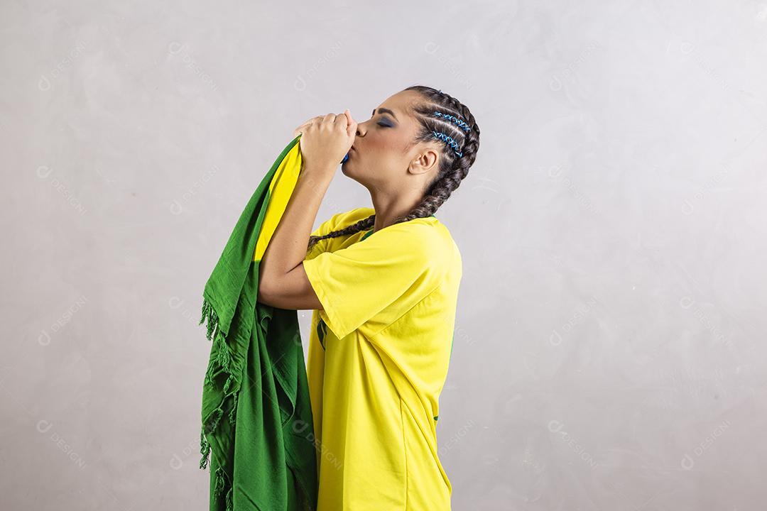 Torcedora brasileira. Fã brasileira beijando bandeira do brasil em fundo cinza.