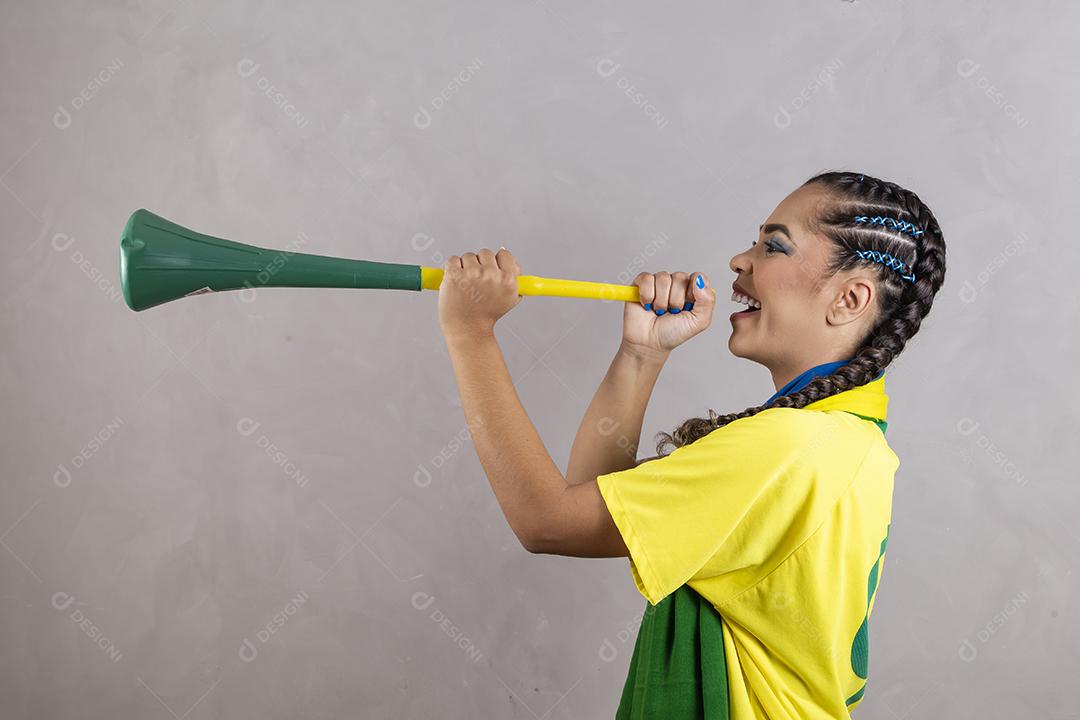 Jovem líder de torcida brasileira com uma vuvuzela em fundo cinza