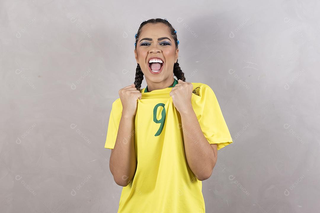 Torcedora brasileira. Fã brasileira comemorando partida de futebol em fundo cinza.