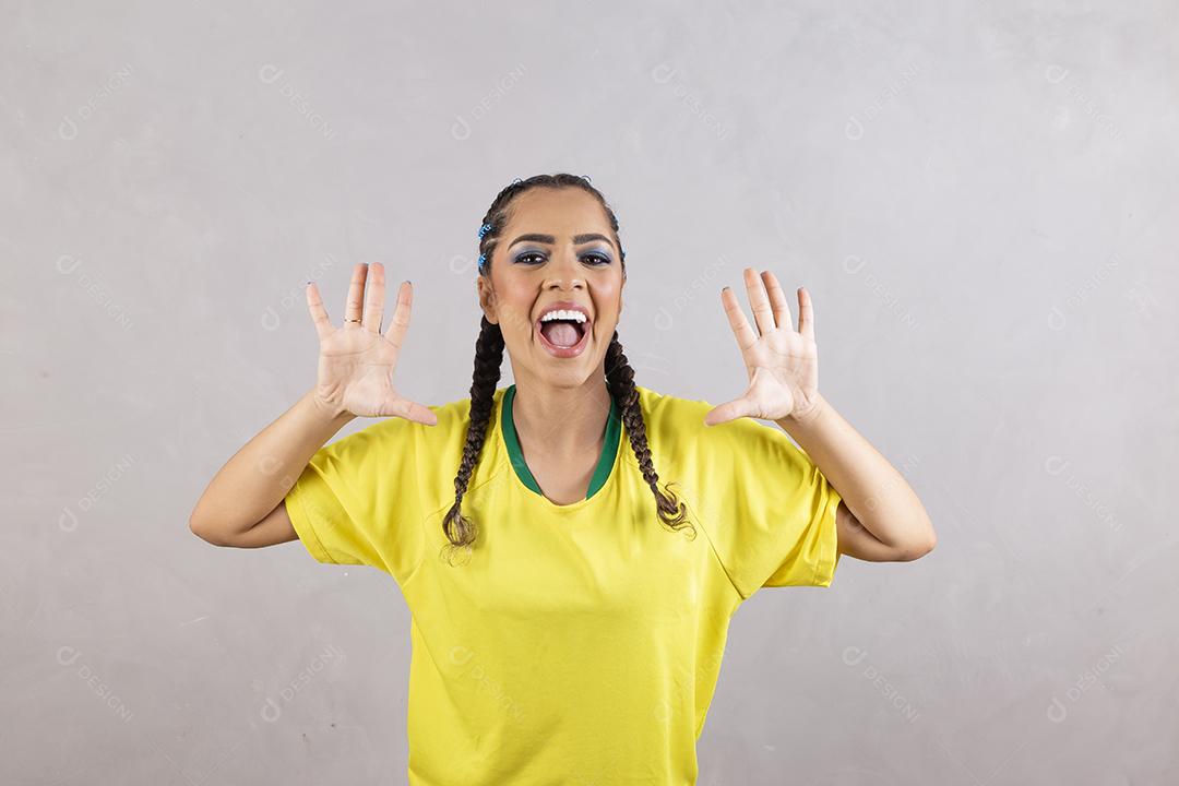 Torcedora brasileira. Fã brasileira comemorando partida de futebol em fundo cinza.