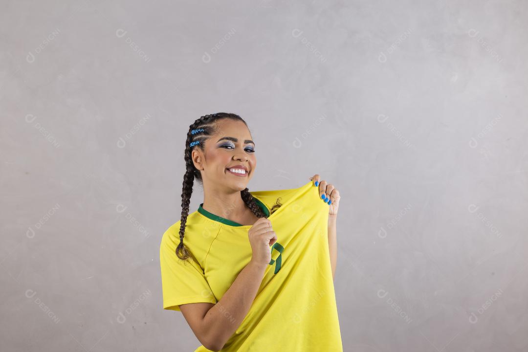 Torcedora brasileira. Fã brasileira comemorando partida de futebol em fundo cinza.