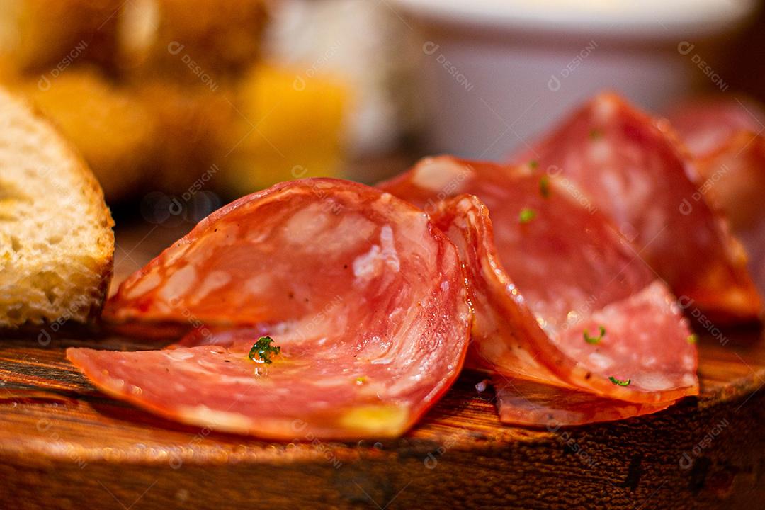 Tabua redonda com petiscos clássicos com close em fatias de salame