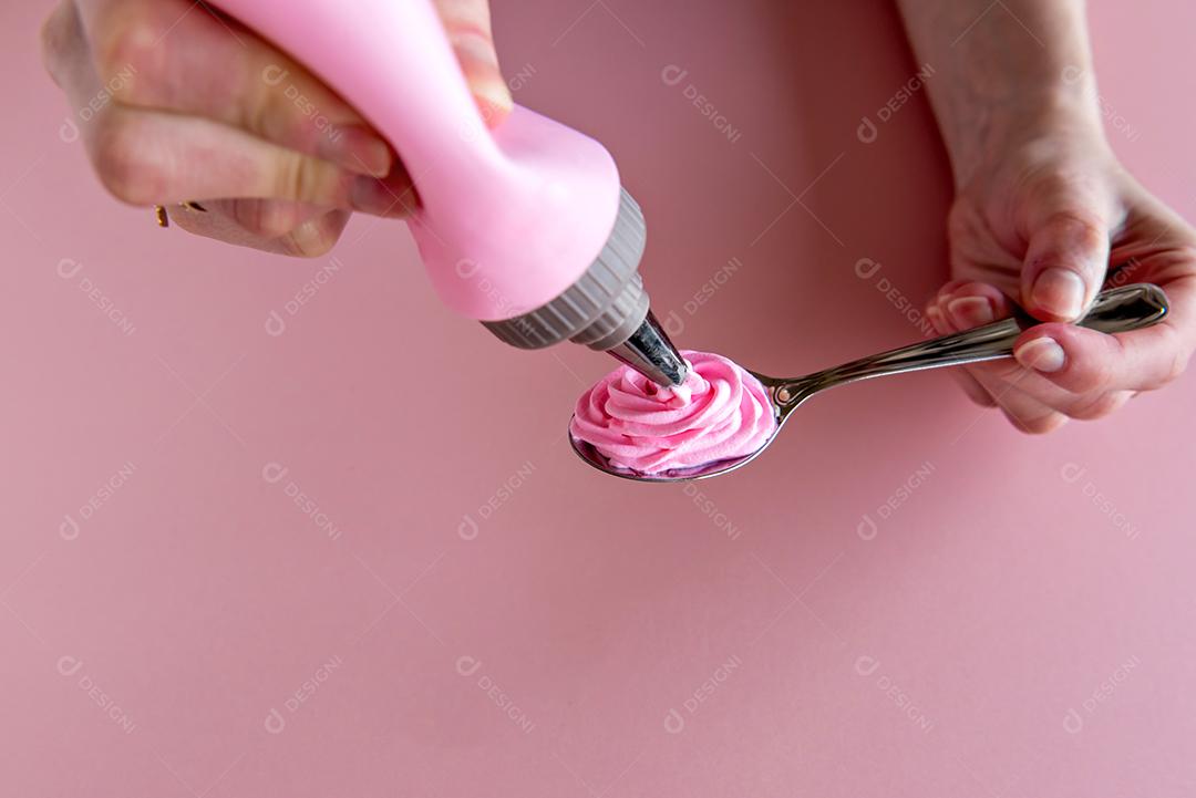 saco de confeitar colocando chantilly rosa na colher.