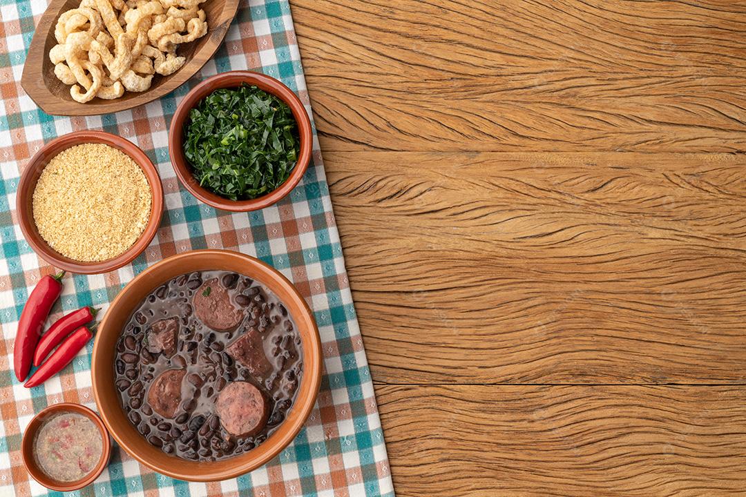 Feijoada brasileira típica com couve, arroz, farofa, torresmos em fundo de madeira