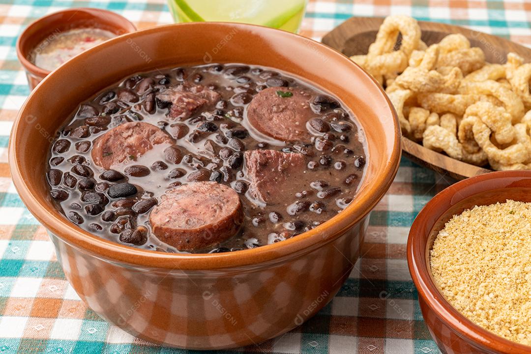 Feijoada brasileira típica com couve, arroz, farofa, torresmos em fundo de madeira