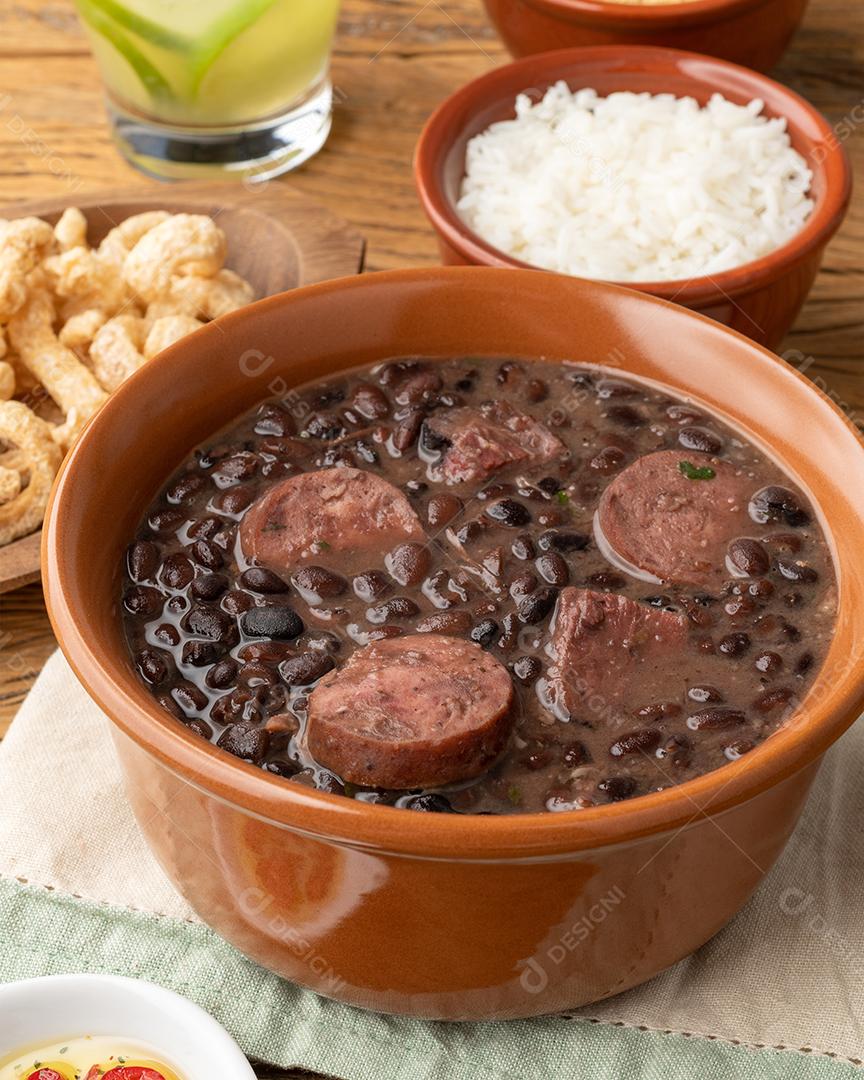 Feijoada brasileira típica com couve, arroz, farofa, torresmos em fundo de madeira