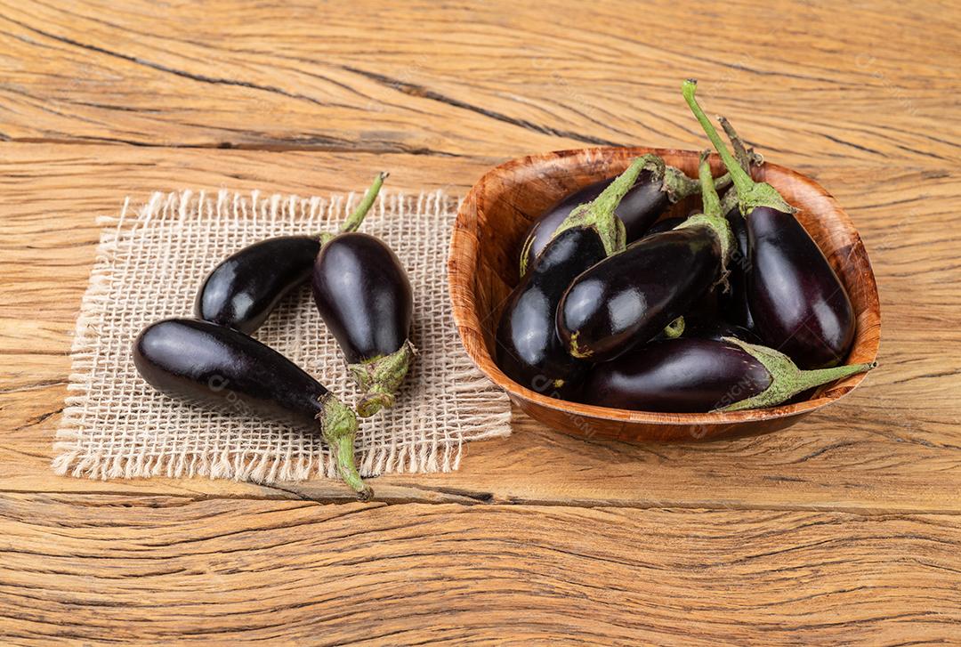 Berinjelas de bebê minúsculo em uma tigela sobre a mesa de madeira.