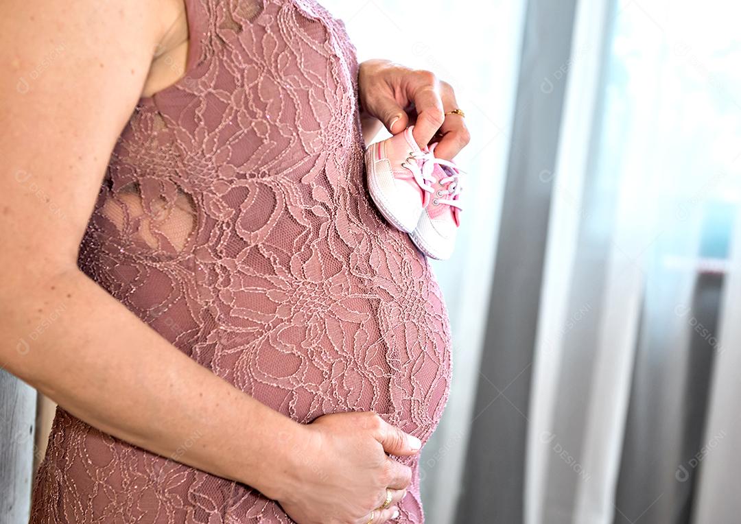 Barriga da mulher grávida segurando o sapato da criança.