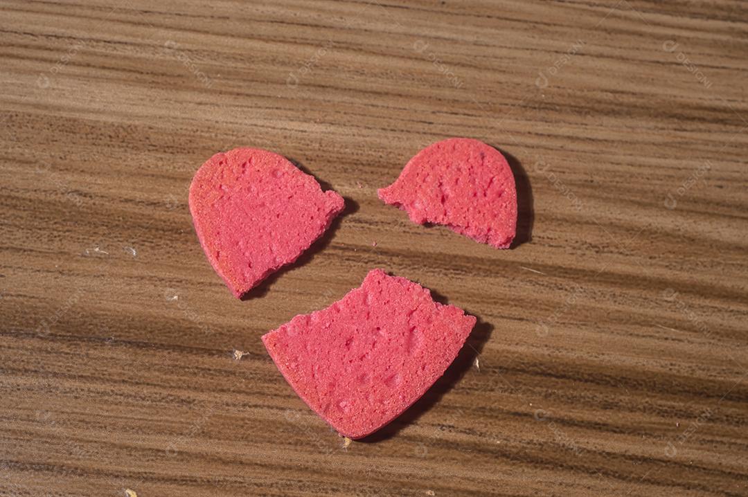 Trabalho de coração partido em pedaços, biscoito em forma de coração partido em uma mesa de madeira.