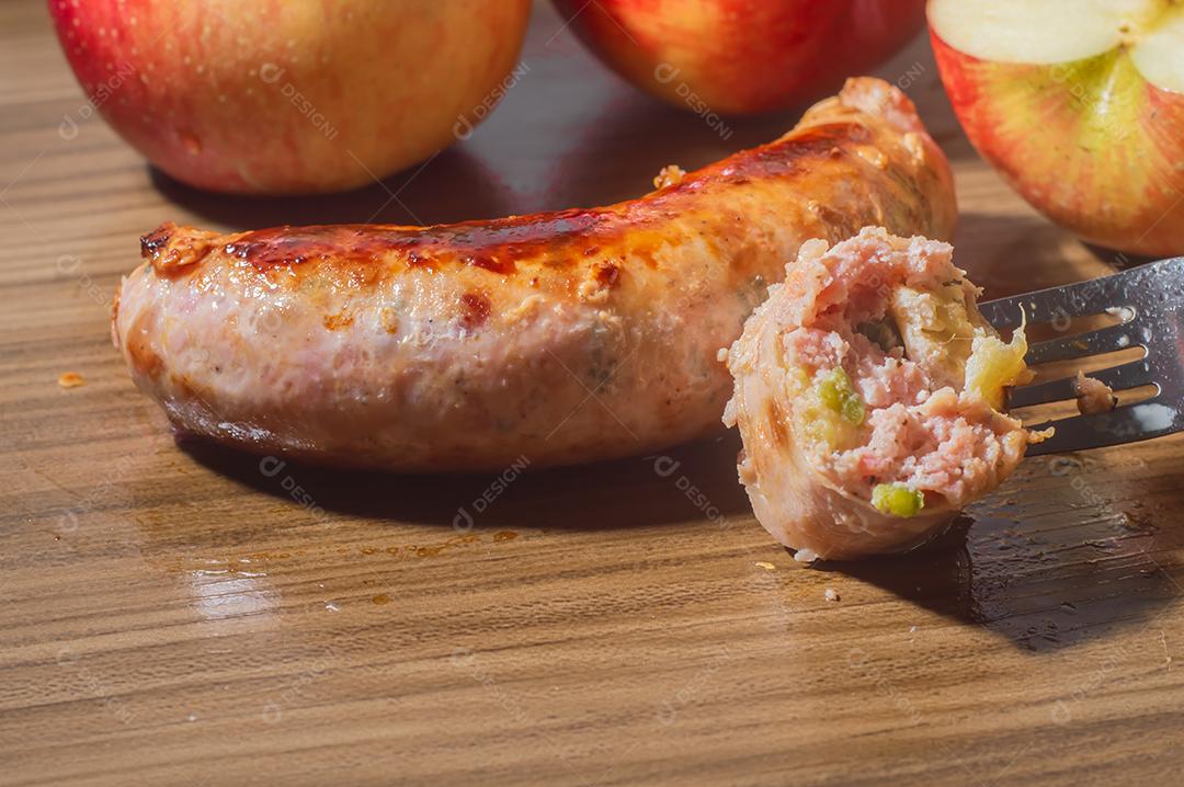 Salsicha feita com maçã e pimenta jaalapeno, em uma tábua de madeira com maçãs