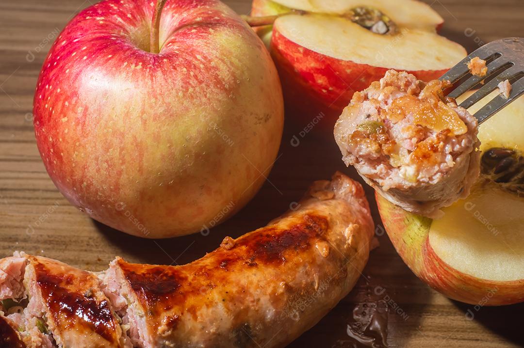 Salsicha feita com maçã e pimenta jaalapeno, em uma tábua de madeira com maçãs