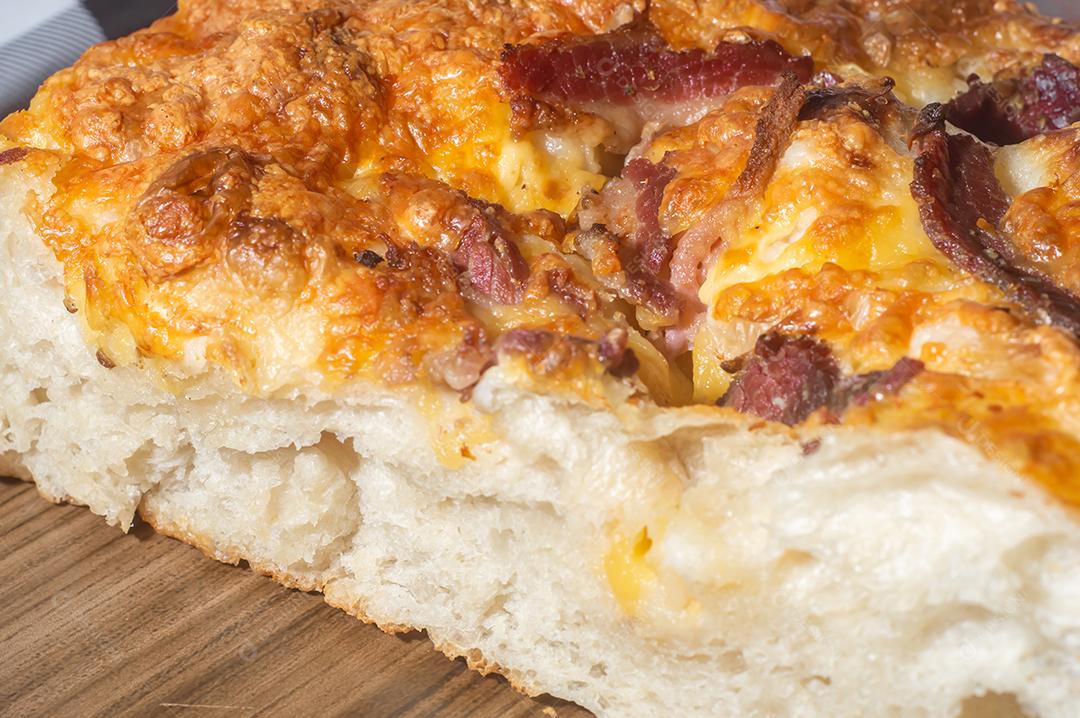 Foccacia italiana recém-assada com queijo amarelo e pastrami, em um tablet de madeira