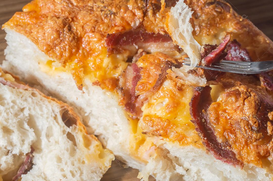 Foccacia italiana recém-assada com queijo amarelo e pastrami, em um tablet de madeira