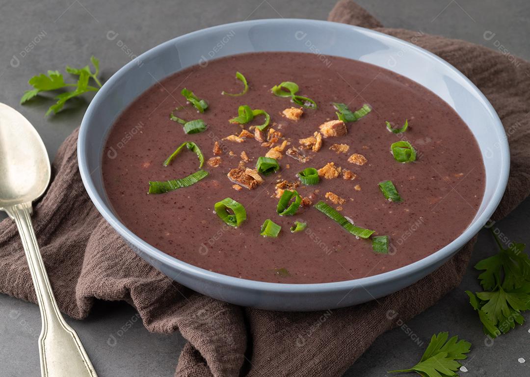 Sopa de feijão preto em uma tigela com tempero sobre fundo de pedra.