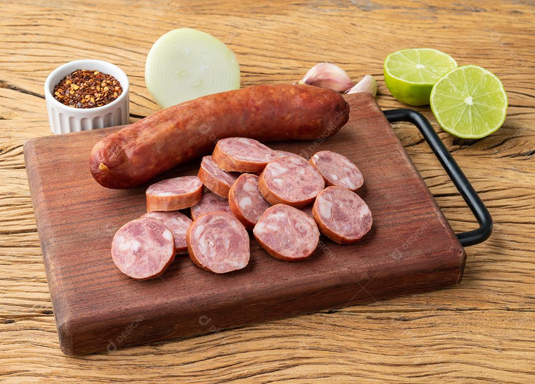 Linguiça de porco calabresa com fatias sobre tábua de madeira com temperos.