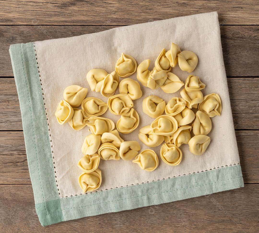 Cappelletti cru ou tortellini sobre um tecido sobre aba de madeira