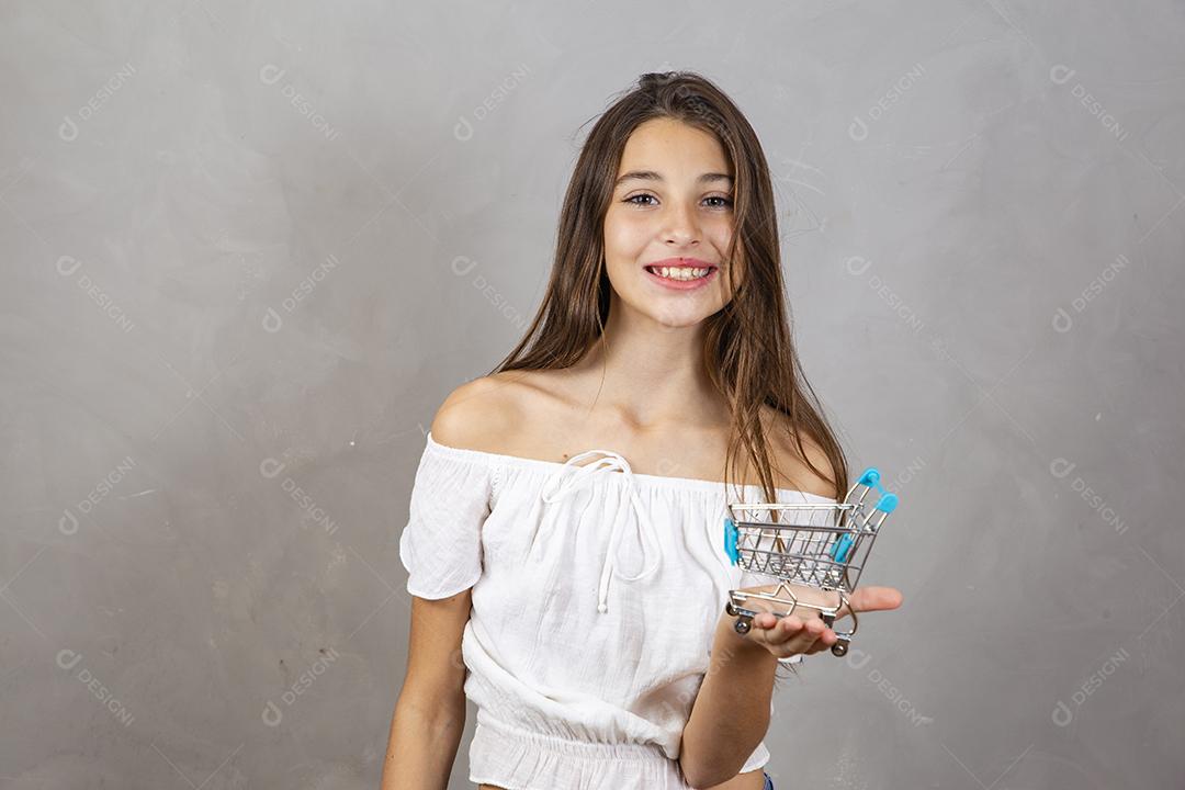 Menina segurando um carrinho de compras em miniatura em fundo cinza Conceito de compras e comércio eletrônico
