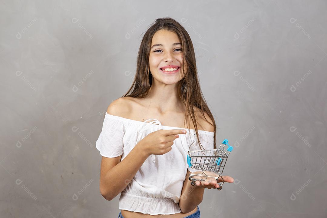 Menina segurando um carrinho de compras em miniatura em fundo cinza Conceito de compras e comércio eletrônico