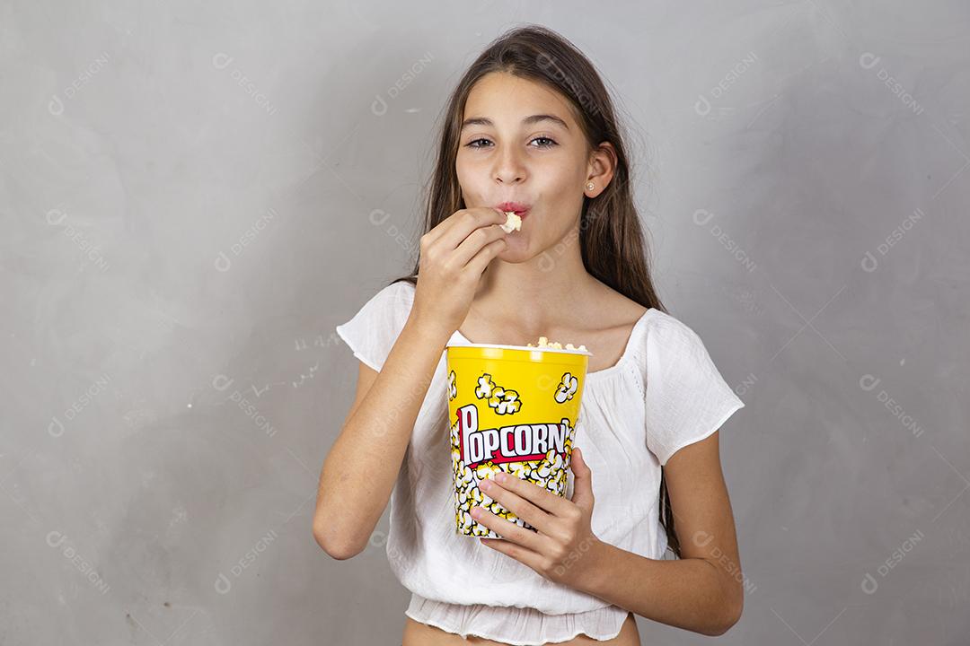 Linda adolescente caucasiana comendo pipoca em fundo neutro com Conceito de entretenimento de férias. menina comendo pipoca